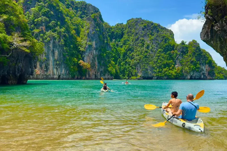 Tourists kayaking in emerald lagoon surrounded by limestone cliffs and green jungle in Koh Lanta kayaking tour